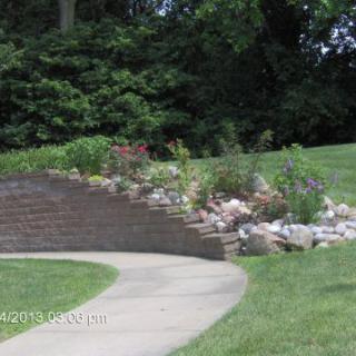 A landscaped garden featuring a stone pathway, brick retaining wall, and various plants.