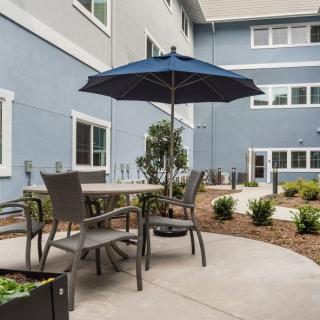 A patio area with a table, chairs, and an umbrella set against a landscaped garden backdrop.