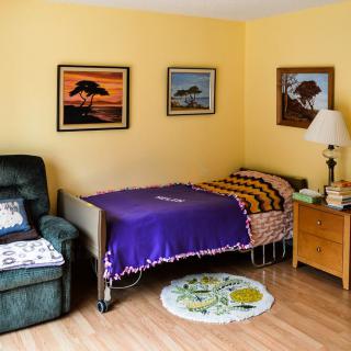 A cozy bedroom featuring a single bed with a colorful blanket, an armchair, and wall art.