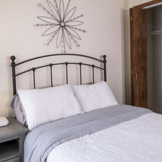 A neatly made bed with white and gray bedding, featuring a decorative metal headboard and wall art.