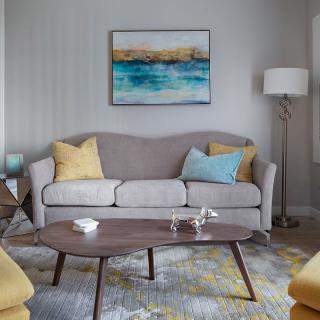 A cozy living room with a gray sofa and colorful pillows, complemented by a wooden coffee table and modern artwork on the wall.