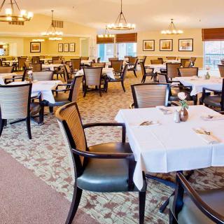 An elegantly furnished dining room with neatly arranged tables and chairs, featuring warm lighting.