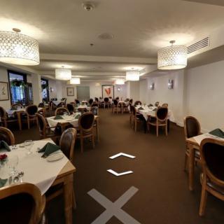 A spacious restaurant dining area with neatly arranged tables and chairs, well-lit by modern hanging lights.