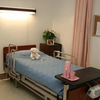 A hospital room featuring a neatly made bed with a teddy bear placed on top.