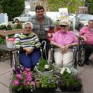 A group of people enjoying a day in the garden with plants and flowers around them.
