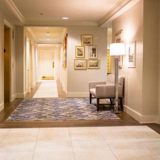 A modern hallway with a patterned carpet and artwork on the walls, featuring a cozy chair and a floor lamp.