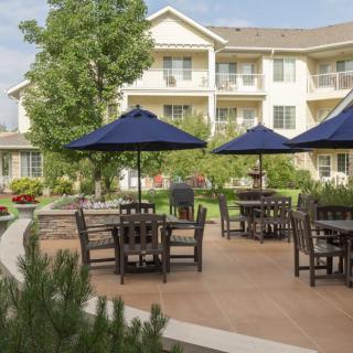 An outdoor patio area with tables, chairs, and blue umbrellas in front of a residential building.