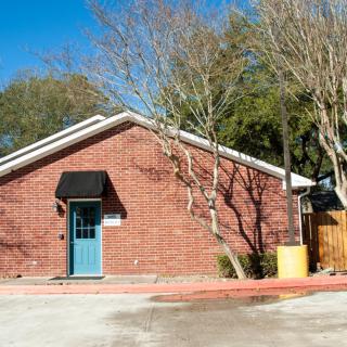 A small brick building with a blue door under a clear blue sky, surrounded by trees.
