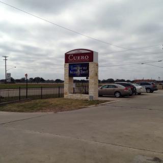 A view of a parking lot with a store sign and several cars under a cloudy sky.
