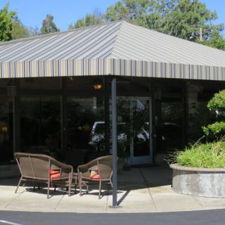 Outdoor seating area of a cafe with an awning and greenery.