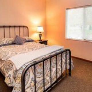 A cozy bedroom with a bed, nightstand, and lamp by the window.