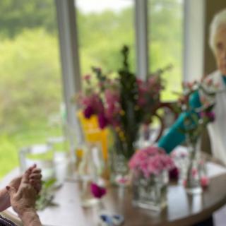 Two people engaged in conversation at a table adorned with flowers by a window.
