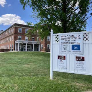 A welcoming sign in front of a brick building on a sunny day.