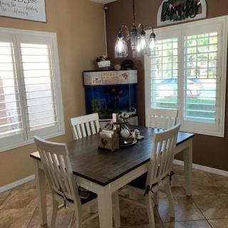 A cozy dining room with a wooden table and chairs, featuring stylish lighting and window shutters.