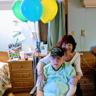 A heartwarming moment of celebration with an elderly person and their caregiver, surrounded by colorful balloons.