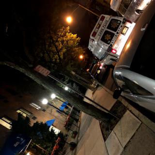 A nighttime view of a city street with parked cars and ambient lighting.