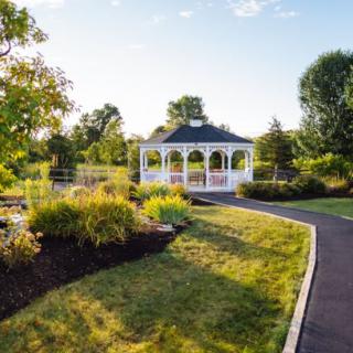 A tranquil garden scene featuring a white gazebo surrounded by lush greenery and a winding pathway.