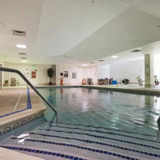 An indoor swimming pool in a fitness center with exercise equipment nearby.