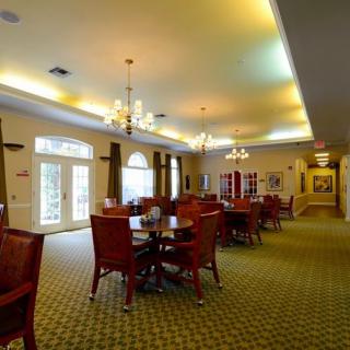A well-lit dining room featuring multiple tables and chairs, adorned with chandeliers and carpet flooring.