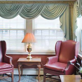 A cozy living room corner with two red armchairs, a small wooden table, a lamp, and elegant draped curtains.