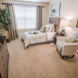 A cozy bedroom with neutral tones, featuring a single bed and an armchair.