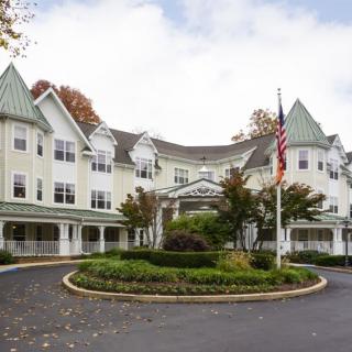 A large, multi-story building with decorative architecture and a well-maintained garden in the foreground, featuring an American flag on a pole.
