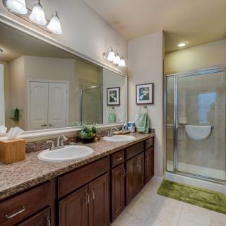 A modern bathroom with a double vanity, large mirror, and glass-enclosed shower.