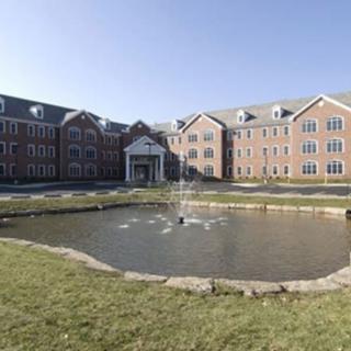 A large brick building with a pond and fountain in front, set in a landscaped area.