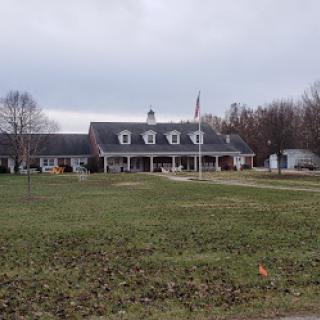 A picturesque residence with a flagpole and expansive green lawn under a cloudy sky.