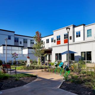 A modern residential building with a landscaped garden and pathway on a sunny day.