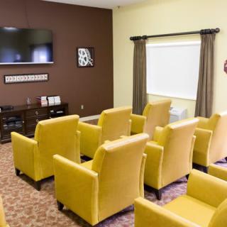 A neatly arranged room with yellow armchairs facing a mounted television.