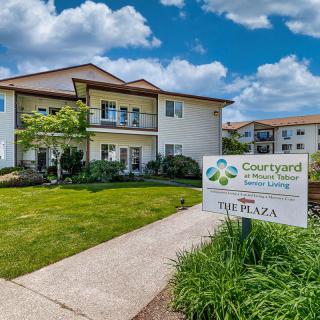 A well-maintained building with a sign for 'Courtyard Senior Living' surrounded by a lush green landscape under a bright blue sky.
