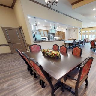 Spacious dining area with a large wooden table and plush chairs, adjacent to an open kitchen.