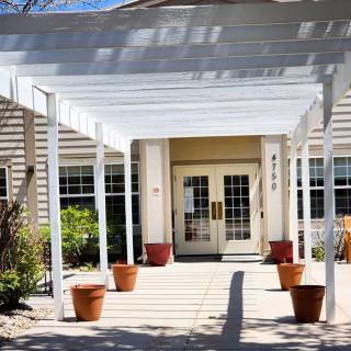 A building entrance with a white pergola and potted plants.
