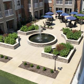 A beautifully landscaped courtyard with a central fountain, surrounded by patio furniture and blue umbrellas.