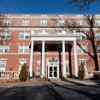 A large brick building with white columns at the entrance, set against a clear blue sky.