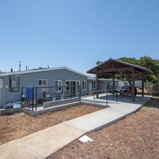 A small house with a paved walkway leading to a covered pavilion in a sunny yard.