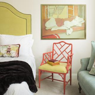 A stylish bedroom featuring a unique red chair, an abstract painting on the wall, and a cozy bed with plush pillows.