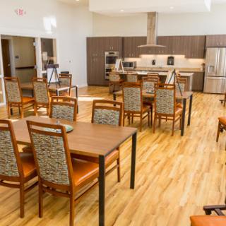 A spacious and modern dining area featuring wooden tables and chairs, with a well-equipped kitchen in the background.