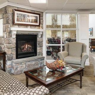 A cozy living room with a stone fireplace, armchair, and a glass coffee table adorned with decorative objects.