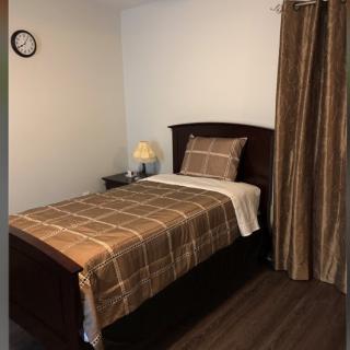 A simple bedroom with a single bed and brown plaid bedding, accompanied by a nightstand, lamp, and wall clock.
