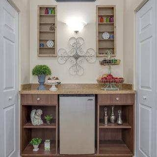 A well-organized kitchen nook featuring a small refrigerator, wooden shelving with decorative items, and wall-mounted cabinets.