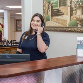 A receptionist smiling while talking on the phone at an office desk.