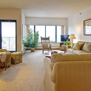 A cozy living room with a beige sofa, rocking chair, and large windows providing natural light.