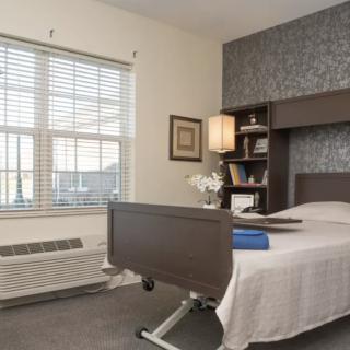A hospital room featuring a bed, bookshelf, and large window.