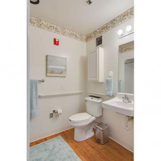 A clean and tidy bathroom with a toilet, sink, mirror, and wooden flooring.