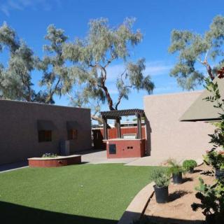 A serene outdoor courtyard featuring artificial grass, brick structures, and lush trees under a clear blue sky.
