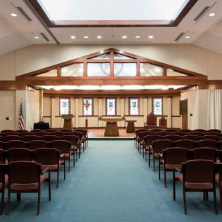 A chapel interior with rows of seats, wooden beams, and large windows.