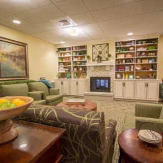 A cozy living room with a fireplace and neatly arranged shelves, featuring comfortable seating and warm decor.