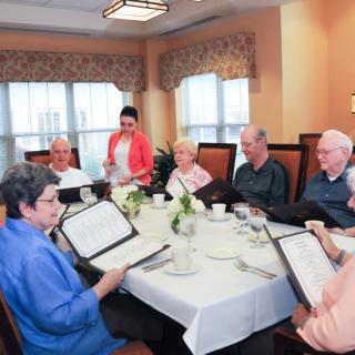 A group of senior citizens enjoying a meal together at a restaurant, browsing menus and engaging in lively conversation.